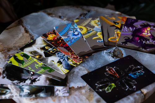 A fan of illustrated Ignisynthia cards spread across a polished marble surface, with one black card showing a crystal cluster design in the foreground.