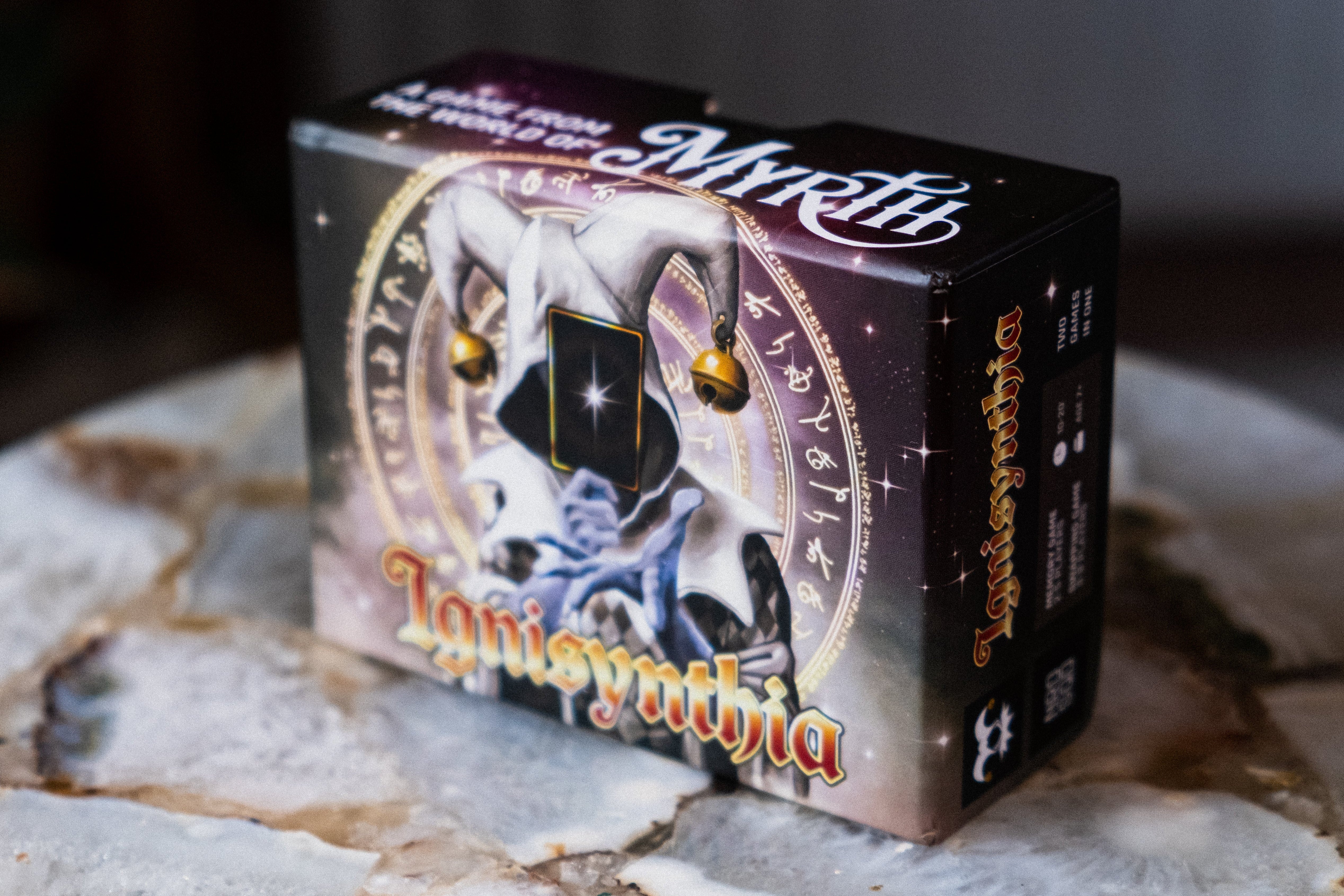 Card game box titled 'Ignisynthia' with decorative elements on a stone surface