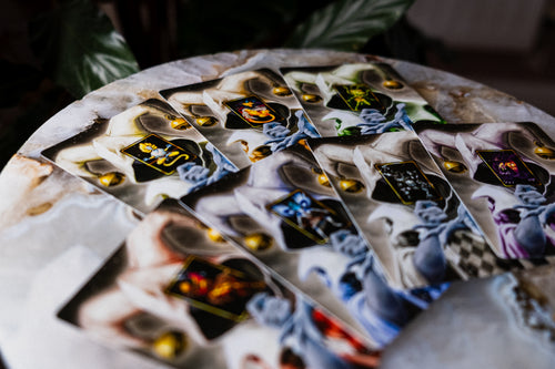A fan arrangement of illustrated Ignisynthia wild cards featuring stylized faces and abstract artwork, photographed on a round stone surface with a blurred dark background.